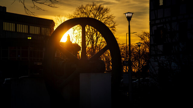 The flywheel of an old steam engine in the rays of the setting sun next to an antique street lamp.