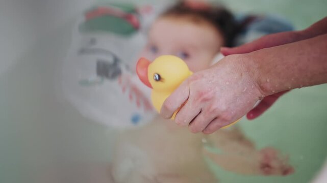 Infant floating in bathtub using inflatable baby bath support during bath time, with a hand holding a yellow rubber duck