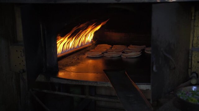 Thin Arabic bread shrak or pita, with lamb meat being cooked inside traditional oven, gas flames over metal plate