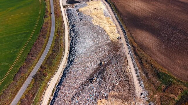 Wide aerial view of large scale municipal solid waste landfill. Drone perspective showing the extent of garbage disposal site adjacent to agricultural land.