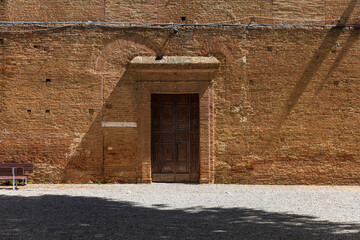 Fototapeta premium Historic Wooden Door in Sunlit Brick Wall, Siena, Italy
