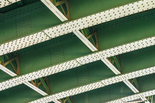 Underside view of a green riveted metal bridge structure with white beams