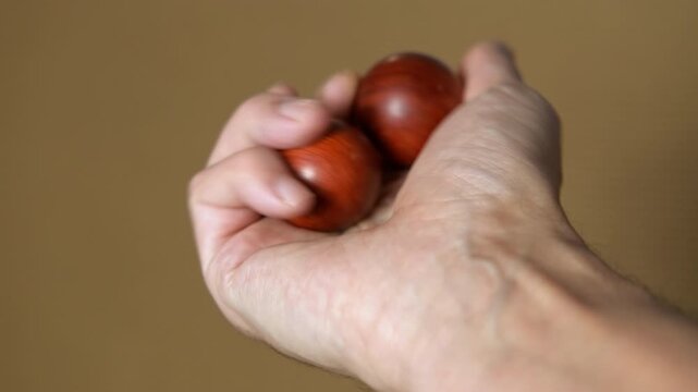 Hand rotating wooden baoding balls for dexterity. Close-up of a person's hand exercising with two wooden baoding balls, rotating them in the palm to improve dexterity, stimulate circulation