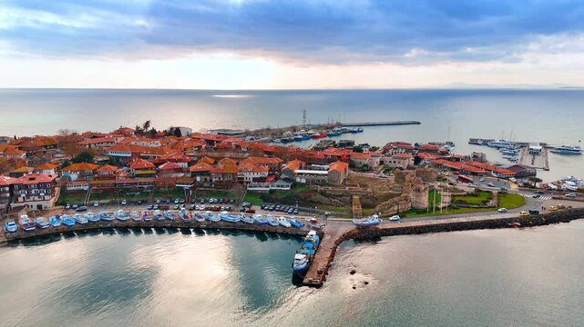 Aerial shot of fishing harbor and ancient ruins seaside. High angle view of a harbor with blue boats and medieval stone ruins near the coast.