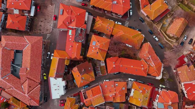 Top down view of red roofs and narrow streets. Aerial shot showing geometric pattern of red tile roofs and small paved city streets.