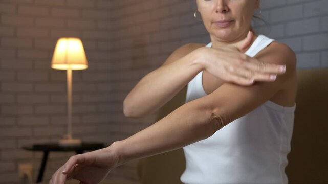 Mature woman using a spiky ball for arm self massage. Middle-aged woman performing a self-massage on her arm with a small spiky ball to relieve muscle tension and pain