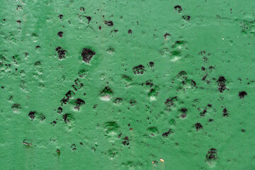 Green painted metal with corrosion texture. Weathered industrial surface with rust spots and decay pattern