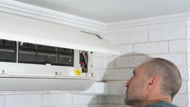 Serviceman repair conditioner indoor. A view of serious service man working with screwdriver in the air conditioner at home