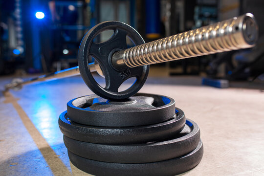 Barbell with weight plates on gym floor close up, strength training equipment in fitness center with blue lighting