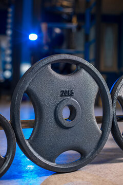 Close up of 5 kg weight plate on barbell in gym, fitness equipment with blue accent lighting
