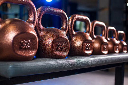 Row of metallic kettlebells on bench in gym close up, fitness equipment with shallow depth of field