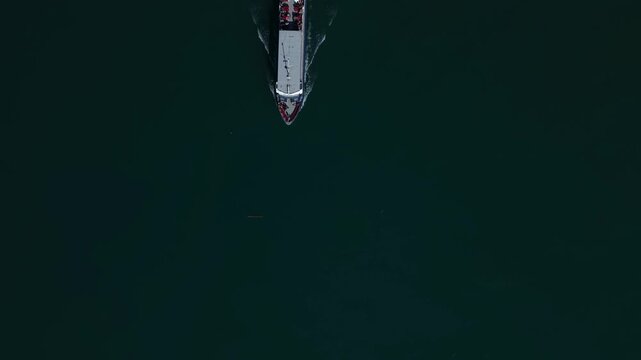Top down aerial view of a passenger ferry moving across a calm alpine lake in Switzerland, creating wave patterns in clear water.