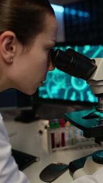 Vertical shot of bicultural young biotech specialists conducting medical research using artificial intelligence software and microscope in modern lab