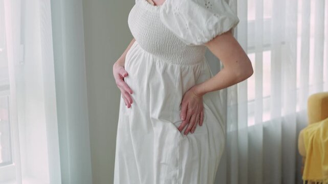 Pregnant woman performing gentle pelvic movements while holding her baby bump at home. Prenatal exercise, labor preparation, healthy pregnancy, childbirth preparation and maternal wellness concept.