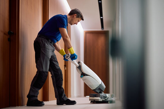 Commercial cleaning worker polishing office corridor with industrial floor scrubber machine.