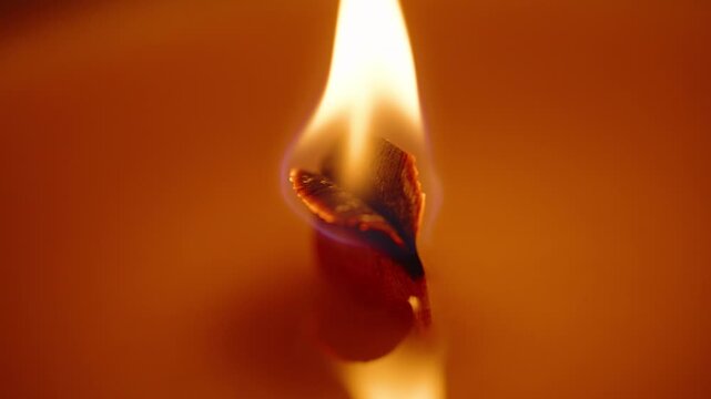 Burning Candle Wick with Flame Twisting Gently in Soft Glow on Orange Wax Surface, Macro Closeup, Aromatherapy Concept