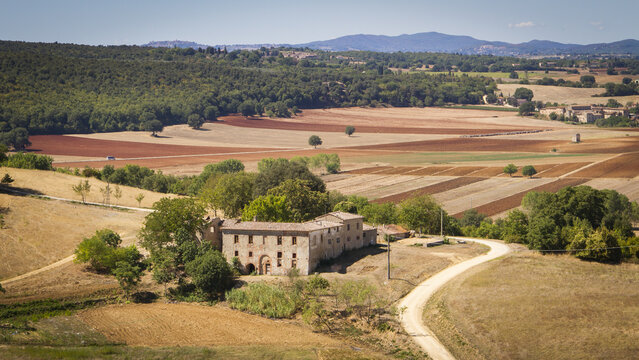 View of rustic stone building with arched entrances sits amidst sun-drenched fields, a tapestry of ochre and umber under a boundless sky, Monteriggioni, Tuscany, Italy.