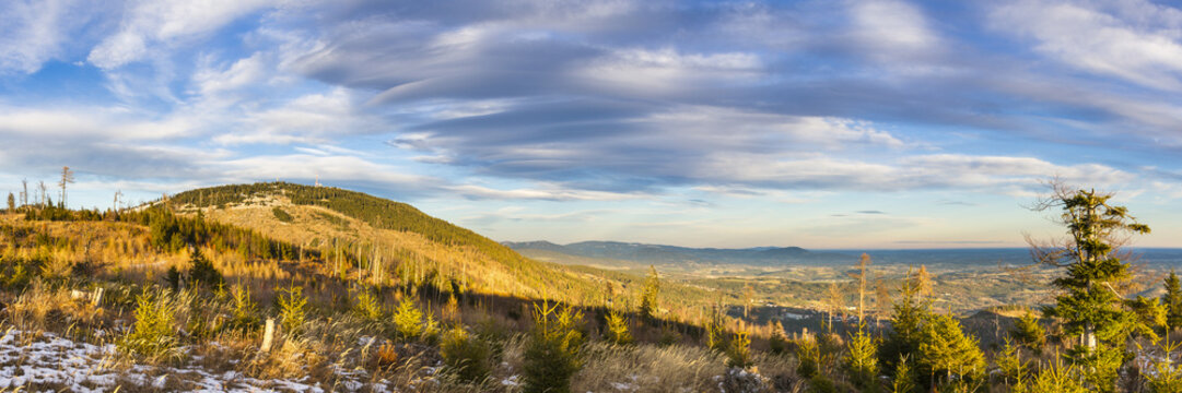 View of golden light paints the rolling hills dotted with evergreens under a vast sky streaked with clouds, Schockl, Styria, Austria.