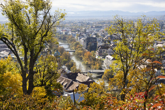 View of the Mur river snaking through the city, with the autumn foliage painting the trees in fiery hues of red, orange, and gold, Graz, Styria, Austria.