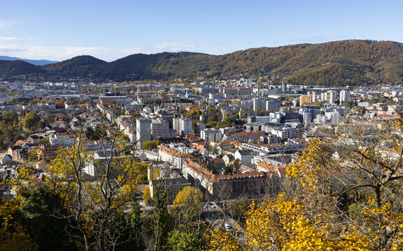 View of autumn tints paint the cityscape with golden hues, nestled amidst rolling hills under a crisp blue sky, a captivating panorama, Graz, Styria, Austria.