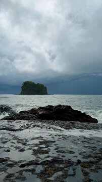 Dramatic ocean view with rocky shore and distant tropical island. Low angle view of wet rocks and tide pools on a tropical beach under a stormy sky in Costa Rica.