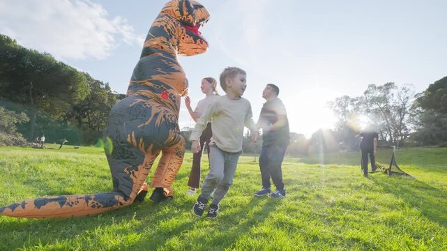 Person in inflatable dinosaur costume chasing children in park