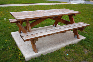 Wooden picnic table with benches on a concrete pad in a public park green area © Life Background