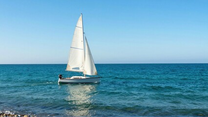 Fototapeta premium Sailboat cruising on calm sea near rocky shoreline