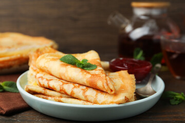 Tasty crepes with jam and mint leaves served on wooden table, closeup © New Africa