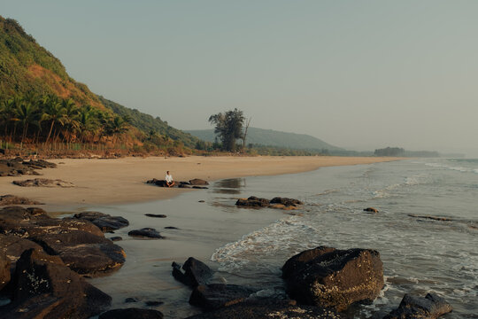 View of the tranquil beach with dark rocks contrasting against the sandy shore, as gentle waves kiss the coastline, Chiplun, Maharashtra, India.