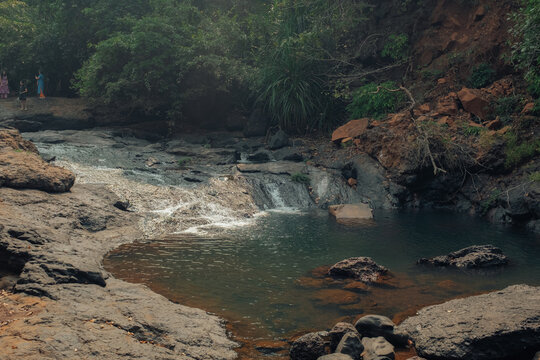 View of cascading waters flow over rocks into a tranquil pool, framed by lush greenery and warm earth tones, creating a serene scene, Chiplun, Maharashtra, India.