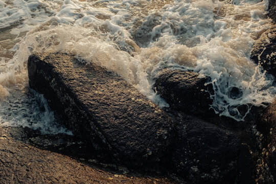 View of frothy, white-capped waves crashing against dark, textured rocks, a dance of nature's raw power and serene beauty, Chiplun, Maharashtra, India.
