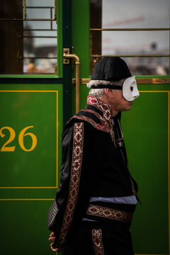 Basel, Switzerland - 10 March 2025: View of a masked figure in traditional attire stands poised against the vibrant green of a passing tram, evoking the festive spirit of Fasnacht..