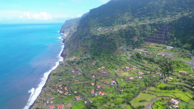 Aerial view of a vibrant Arco de Sao Jorge coastal village on Madeira, Portugal, with terraced fields meeting the turquoise Atlantic. A serene blend of nature and human settlement.