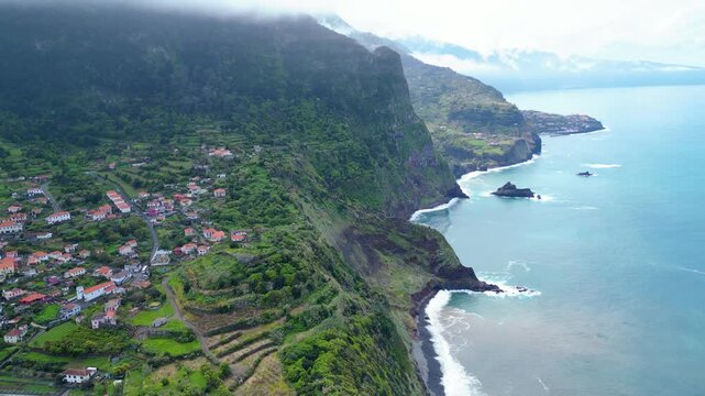 Aerial view of a vibrant Arco de Sao Jorge coastal village on Madeira, Portugal, with terraced fields meeting the turquoise Atlantic. A serene blend of nature and human settlement.