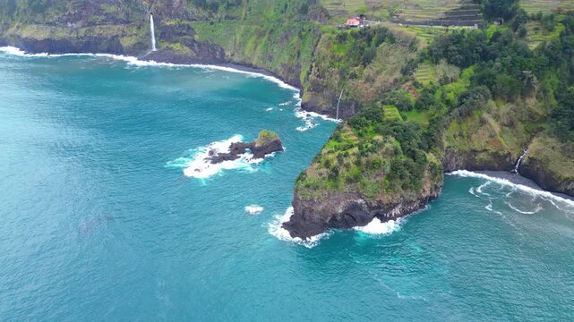 Aerial view of a Seixal coastal village nestled on Madeira's lush green terraces, overlooking the Atlantic. Clouds hug the mountains, creating a dramatic, serene landscape.