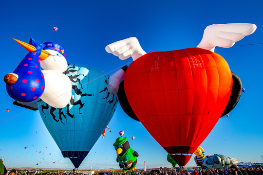 Albuquerque, United States - 12 October 2017: View of whimsical hot air balloons rising against a vibrant blue sky, their vivid colors and playful shapes creating a spectacle of joy.