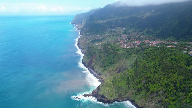 Aerial view of Madeira's dramatic north coast, where lush green terraces meet the Atlantic's deep blue, dotted with charming villages. A vibrant island landscape. Arco de Sao Jorge