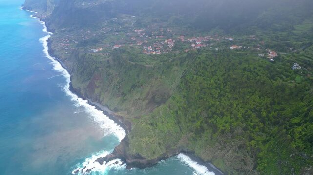 Aerial view of Madeira's dramatic north coast, where lush green terraces meet the Atlantic's deep blue, dotted with charming villages. A vibrant island landscape. Arco de Sao Jorge