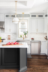 A kitchen detail with gold pendant lights, stainless steel apron sink, white cabinets and large...