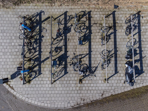 Aerial view of bicycles neatly parked in a structured rack casting long shadows on the patterned pavement, Delft, Netherlands.