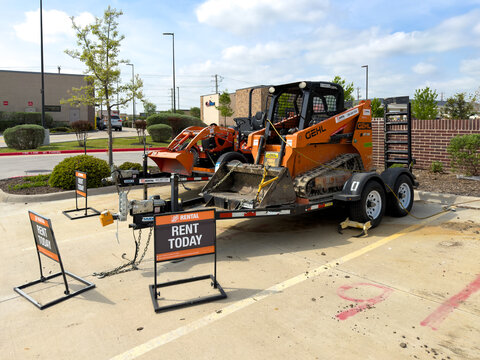 Prosper, Texas, USA - April 1st, 2026: Orange Gehl track skid steer loader sitting on black metal rental trailer in sunny asphalt equipment lot