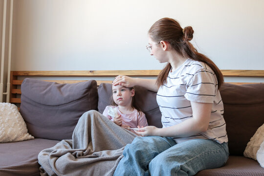 Mother sitting on a couch and taking care of her sick child wrapped in a blanket. Concept of parenting, illness, support, and home healthcare.