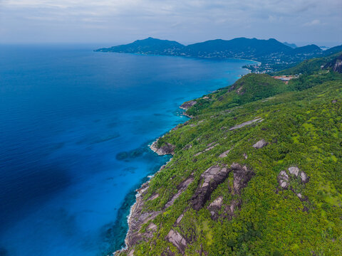 Aerial view of the coastline where lush green hills meet the deep blue sea in a stunning display of natural beauty, Montagne Jasmin, Mahe Island, Seychelles.