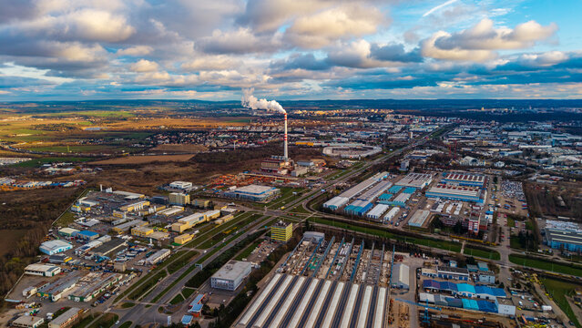 Aerial view of a towering industrial chimney ejecting white plumes against a backdrop of sprawling factories and buildings, Praha, Hlavni mesto Praha, Czechia.