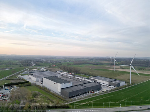 Aerial view of industrial buildings casting long shadows in the fading light, windmills standing tall against the horizon, Ath, Wallonia, Belgium.