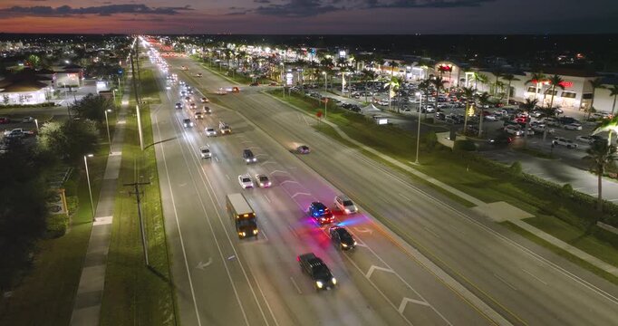 Law enforcement officer conduct nighttime traffic stop for speeding car on American city street. Police lights flashing amid urban traffic.
