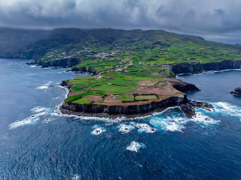 Aerial view of verdant cliffs meet the turbulent Atlantic, the island's edge a tapestry of emerald fields and rugged coastline, Flores, Acores, Portugal.