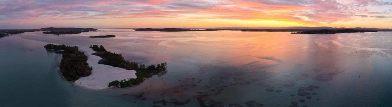 Aerial view of islands stand as silent witnesses to the dawn's embrace, where the sky's fiery hues meet the tranquil waters, Newcastle, New South Wales, Australia.