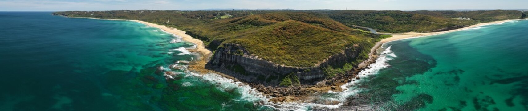 Aerial view of deep turquoise waves crashing against the rugged coastline and sandy beaches, contrasting with the lush green headland, Newcastle, New South Wales, Australia.